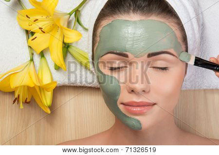 Beautiful girl with a towel on her head applying facial clay mas