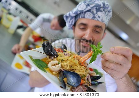 Handsome chef dressed in white uniform decorating pasta salad and seafood fish in modern kitchen