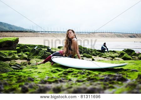 Attractive caucasian girl resting on moss rock after surf session, surf camp in spain