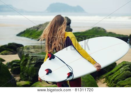 Blond long-haired surfer girl walking to the ocean holding her surfboard