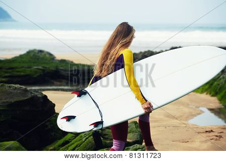 Professional female surfer walking to the ocean waves holding her surfboard