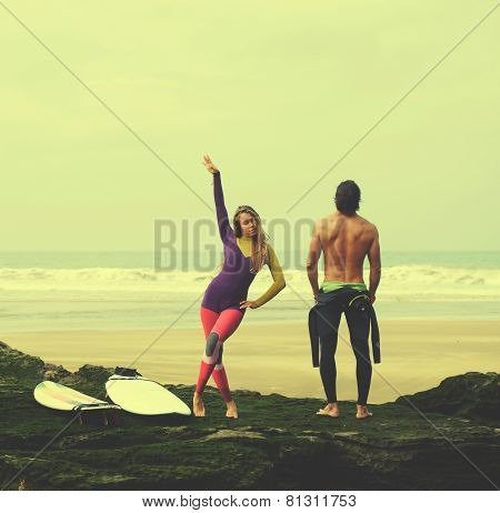 Couple of young professional surfers having fun standing against amazing ocean view filtered image