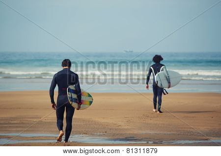 Two surfers carrying their surfboards while going to the sea professional surfers in diving suits.