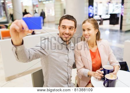 sale, shopping, consumerism, technology and people concept - happy young couple with smartphone taking selfie at cafe in mall