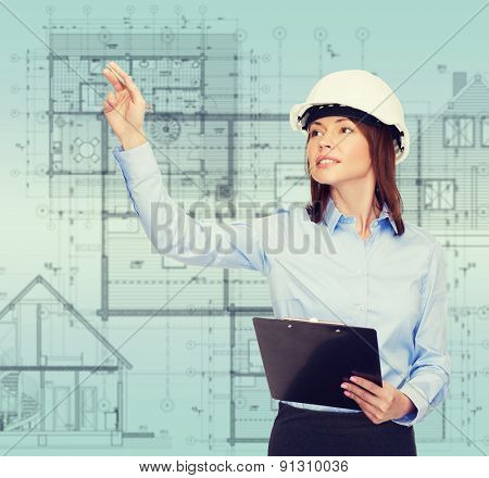 building, developing, consrtuction and architecture concept - smiling businesswoman in white helmet with clipboard pointing finger