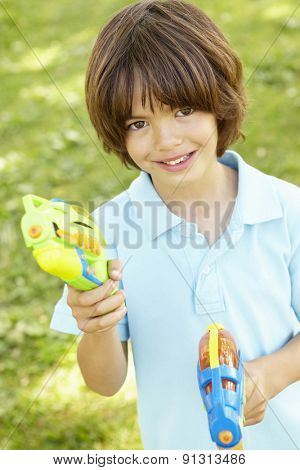 Young Boy Playing With Water Pistols In Park