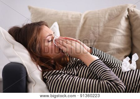 Portrait of a sick woman blowing her nose while sitting on the sofa