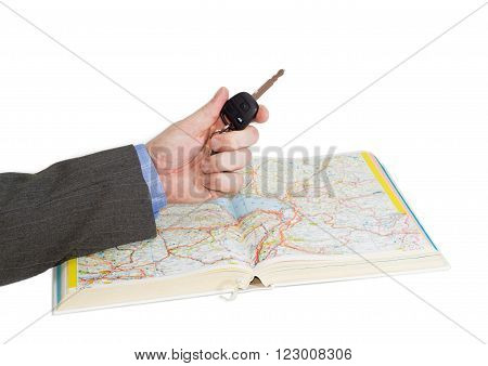 Male hand with car key over an open old road atlas on a light background