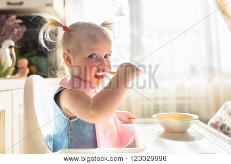 Naughty funny with bunches baby eating independently alone in the high chair light lifestyle