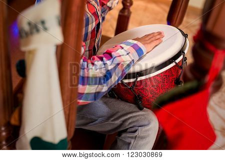child playing percussion drum. Boy plays djembe on stairs. Lively Christmas music at home. Little musician's holidays.