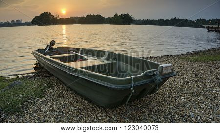 a green boat at the shore of a lake on sunset