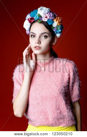 Beautiful model with a wreath of flowers on her head on red background. Beauty Woman face Portrait. Beautiful Spa model Girl with Perfect Fresh Clean Skin.