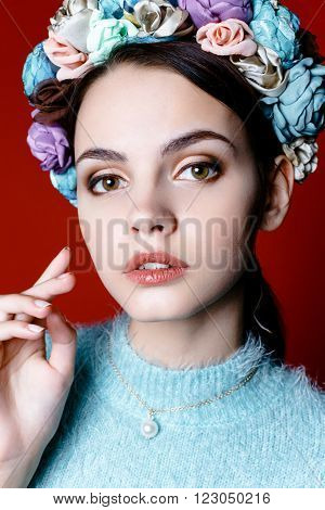 Beautiful model with a wreath of flowers on her head on red background. Beauty Woman face Portrait. Beautiful Spa model Girl with Perfect Fresh Clean Skin.