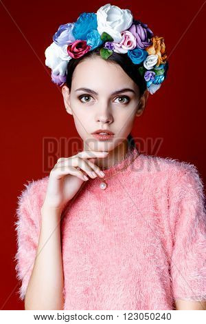 Beautiful model with a wreath of flowers on her head on red background. Beauty Woman face Portrait. Beautiful Spa model Girl with Perfect Fresh Clean Skin.