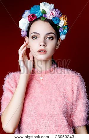 Beautiful model with a wreath of flowers on her head on red background. Beauty Woman face Portrait. Beautiful Spa model Girl with Perfect Fresh Clean Skin.