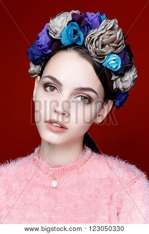 Beautiful model with a wreath of flowers on her head on red background. Beauty Woman face Portrait. Beautiful Spa model Girl with Perfect Fresh Clean Skin.