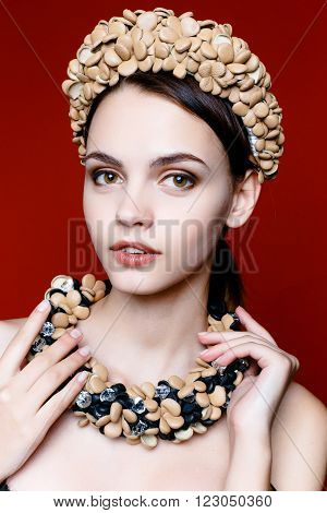Beautiful model with a wreath of flowers on her head on red background. Beauty Woman face Portrait. Beautiful Spa model Girl with Perfect Fresh Clean Skin.