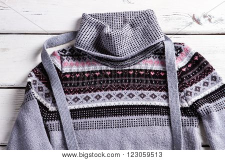 Woman's pullover with small ornament. Gray pullover on white table. Piece of clothing with ornament. Trendy sweater with folded collar.