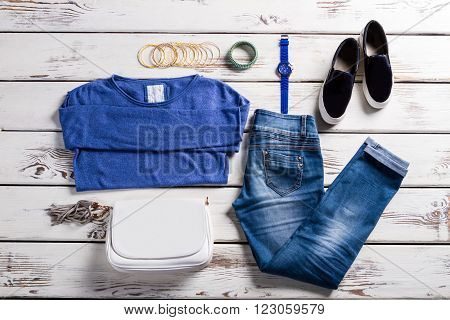 Woman's blue pullover with accessories. Outfit and purse on showcase. Old shelf with new clothes. Lady's simple clothes and accessories.