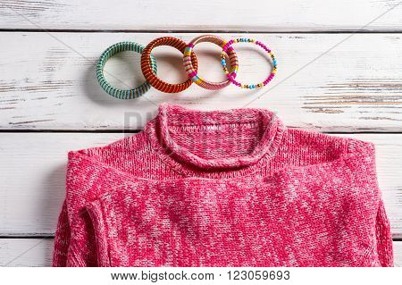 Pink wool pullover and bracelets. Bright pullover on store showcase. Close-up of bracelets and sweater. High-quality clothes in magazine.