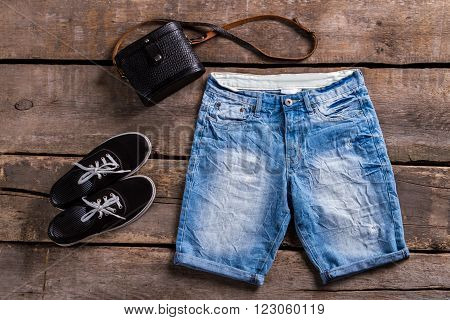 Lady's long blue denim shorts. Female clothing on aged shelf. Classic purse with denim shorts. Black keds and vintage handbag.