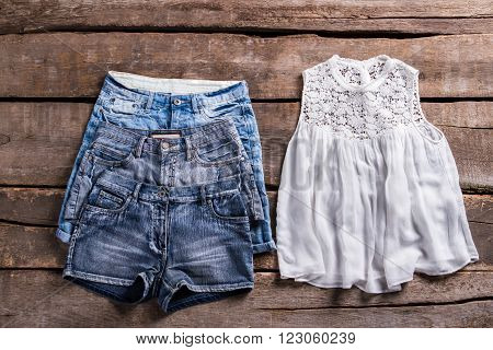 Different denim shorts and top. Woman's clothes on old floor. Light clothing at vintage store. Retro shelf with lady's garments.