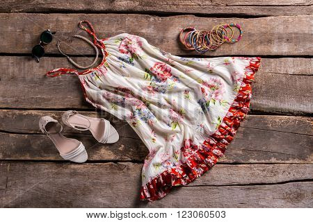 Sarafan with footwear and accessories. Female outfit on brown shelf. Old table with lady's clothing. Vintage sarafan with colorful bracelets.