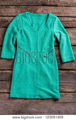 Turquoise dress with zipper pockets. Tuquoise dress on old shelf. Garment on aged wooden background. Woman's high-quality clothing.