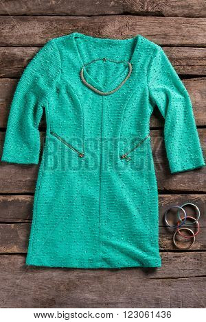 Turquoise dress and necklace. Clothes on brown wooden backround. Retro shelf with bright dress. Modest clothing and small accessories.