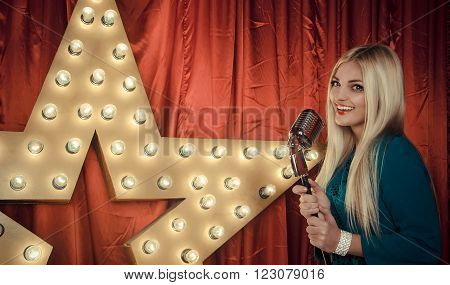 Portrait of beautiful young woman singing on stage with microphone with star on the wall