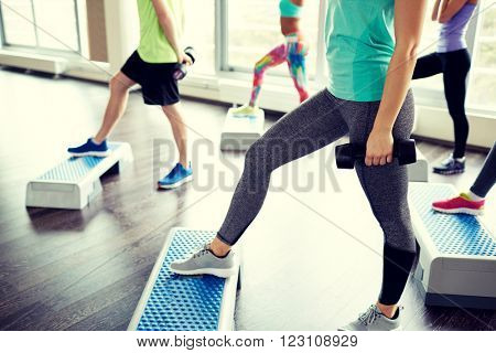 fitness, sport, aerobics and people concept - group of smiling people working out with dumbbells flexing muscles on step platforms in gym
