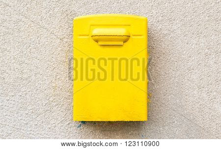 Yellow post office mailbox on plastered wall with paint splashes in blue and yellow colors