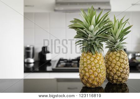 A two whole pineapples sitting on a kitchen bench