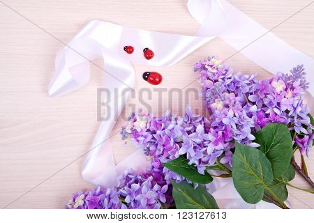 Bunch of violet lilac with ladybirds and white tape on a wooden background