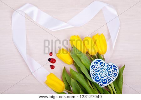 Bouquet of yellow tulips and ornamental openwork heart heart on a wooden background