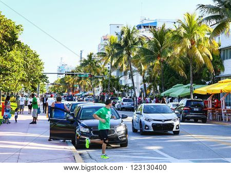MIAMI BEACH, USA - MAY 9, 2015: Cars driving and parking people walking by or running street cafes with sunshades on the side of the Ocean Drive.