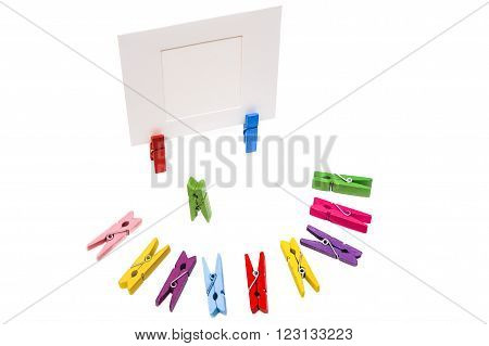 Green clothespin stands in the center. Colored pegs lie in a semicircle. Two clothespins holding white frame