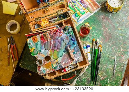 Bright workplace of the artist with brushes, oil paints, pallete, palette knife and tea with lump sugar