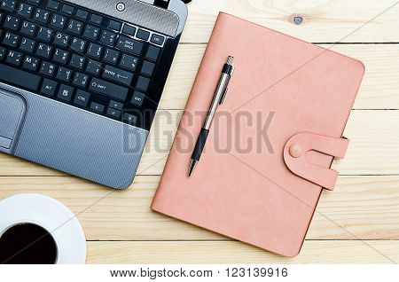 Leather notebook with pen cup of coffee and labtop on office desk.Top view