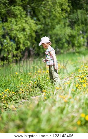 Girl in cap standing on a forest path looking at dandelions
