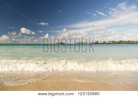 Beautiful marine view on sea coast line with clean wavy surf water on sandy beach with lighthouse on horizon and cloudy blue sky horizontal picture