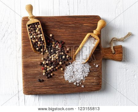 Salt and pepper in wooden shovels on wooden cutting board top view