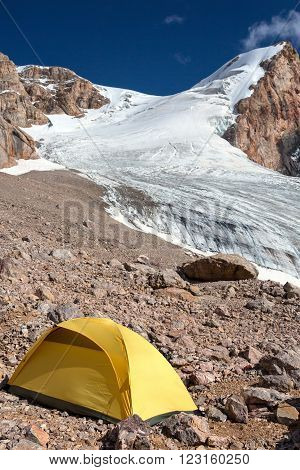 Mountain View with Ice Glacier and Peaks on Background and Small Single Alpine Yellow Tent located on Rocky Moraine on Foreground