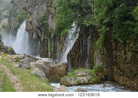 Kapuzbashi waterfalls down to river. Lush vegetation on rock surface surround waterfalls. Turkey Aladaglar mountains.