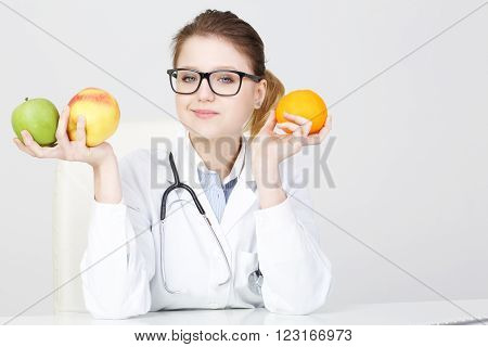 young beautiful female dietitian holding apples and an orange.