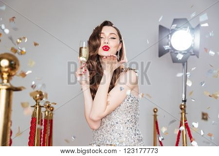 Lovely woman holding glass of champagne and blowing kiss at amera