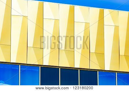 Kristianstad Sweden - March 20 2016: Golden abstract detail of a facade with windows below. Blue reflections and blue sky. Galleria Boulevard shopping mall in the city.