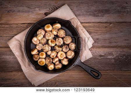 Garlic mushrooms cooked in a cast iron skillet, resting on greaseproof paper on old table. Overhead view with retro style processing.
