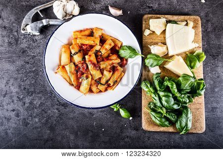 Italian and Mediterranean cuisine. Pasta Rigatoni with tomato sauce basil leaves garlic and Parmesan cheese. An old home kitchen with old kitchen utensils.