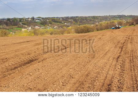 Tractor In Ploughed Field By Forest Ukrainian Village On Hills